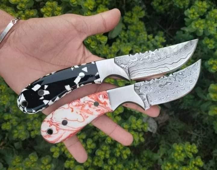 Damascus bull cutter knife with a resin handle and steel bolster beside a leather sheath