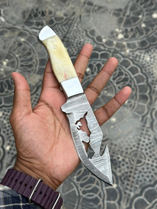 Damascus belt knife with a camel bone handle and steel bolster beside a leather sheath