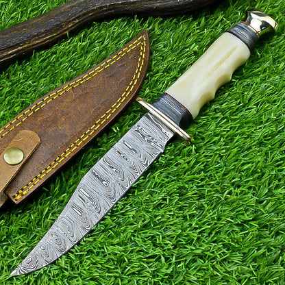 Damascus Western camp knife with a camel bone handle and metal guard beside a leather sheath
