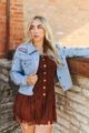 Woman in a light wash denim jacket with concho buttons over a brown suede dress