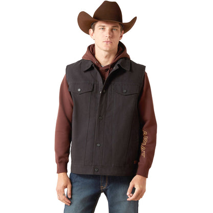 Man in a black canvas Ariat rancher vest over a maroon hoodie, jeans and a brown cowboy hat